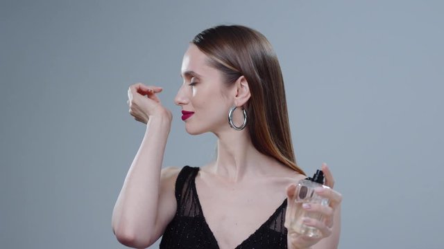 Beautiful woman spraying perfume on her neck beauty bottle elegant glamour in studio model grey background hand use flavor girl skin young aroma inside luxury portrait close up slow motion