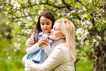 Obraz premium Happy woman and child in the blooming spring garden.Child kissing woman. Mothers day holiday concept