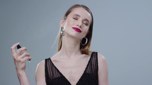 Young woman spraying perfume on her neck beauty bottle elegant glamour in studio model grey background hand use flavor girl skin young aroma inside luxury portrait close up slow motion