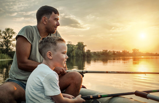 Happy Father And Son Together Fishing From A Boat At Sunset Time