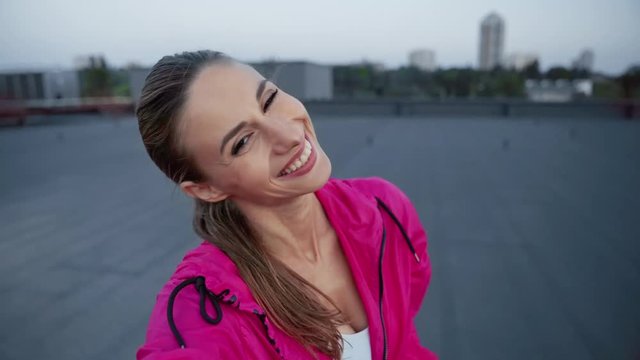 charming sportswoman in sportswear waving hello, talking at video chat, holding smartphone in hands and standing on rooftop
