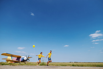 Obraz na płótnie Canvas Cute Caucasian teenage couple dressed in blue and yellow outfit holding hands and running outdoors with balloon.