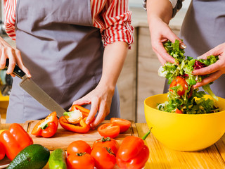 Vegetarian home recipe. Cropped shot of women cooking together, preparing salad. Lady cutting red bell pepper.