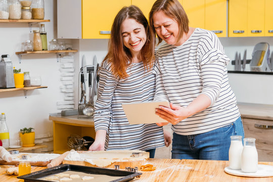 Family leisure. Mother and daughter using tablet to watch fun cooking video tutorial in kitchen.
