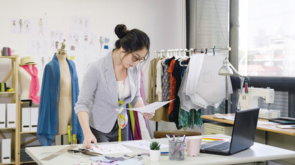 elegant female designer working on laptop and sketching at desk in studio. young woman fashion...