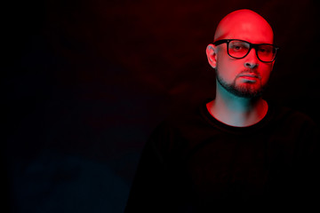 Attractive bald man with beard in glasses on neon light background