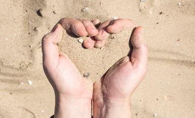 women's hands holding sand in his hands in the shape of a heart,the concept of life running out like sand through fingers