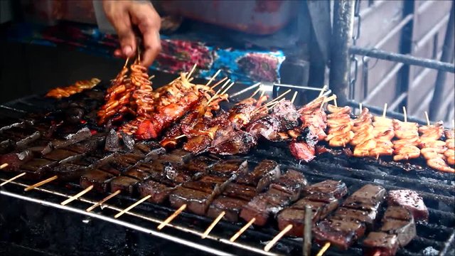 Close up handheld video shot of chicken and pork innards on a barbecue grill