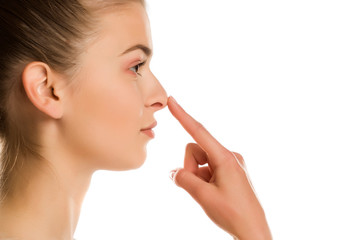 profile of young woman touches her nose on white background