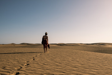 evocative image of young confident woman with dress walking alone on desert sand among dunes on a...