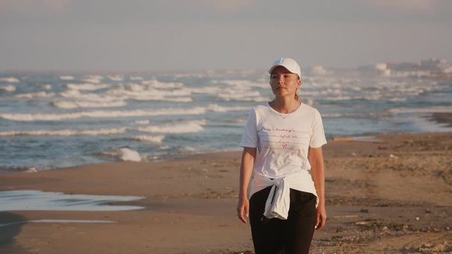 Young woman in good mood walks along the ocean beach and enjoys morning sun and fresh air. Happy calm harmony