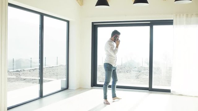 Mature man with smartphone in unfurnished house, moving in new home concept.