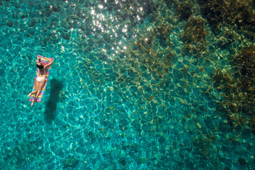 aerial view of a beautiful young woman in bikini on a matress in the sea