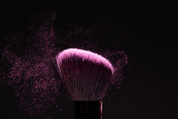 Make up brush with pink powder splashes on black background.