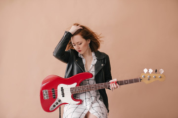 Young beautiful woman posing with red bass guitar in a studio - obrazy, fototapety, plakaty