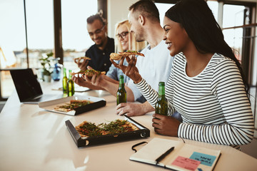 Smiling African American businesswoman having pizza and beers with coworkers