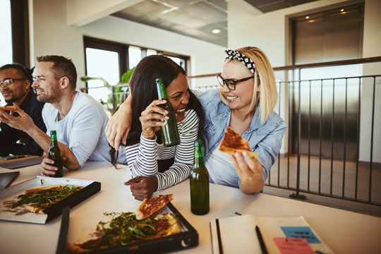 Two businesswomen laughing over beers and pizza after work