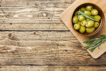 Green olives in wooden bowls on wooden table. Top view with space for text.