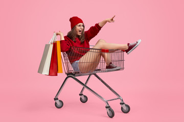 Young woman with paper bags riding shopping cart