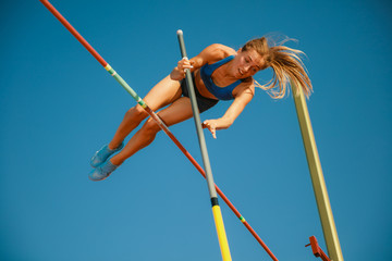 Professional female pole vaulter training at the stadium in sunny day. Fit female model practicing in high jumps outdoors. Concept of sport, activity, healthy lifestyle, action, movement, motion.