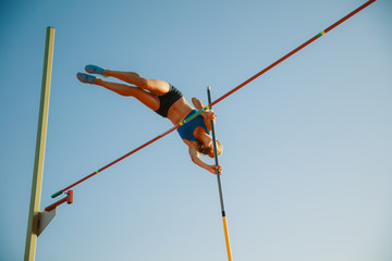 Professional female pole vaulter training at the stadium in sunny day. Fit female model practicing...