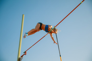 Professional female pole vaulter training at the stadium in sunny day. Fit female model practicing...