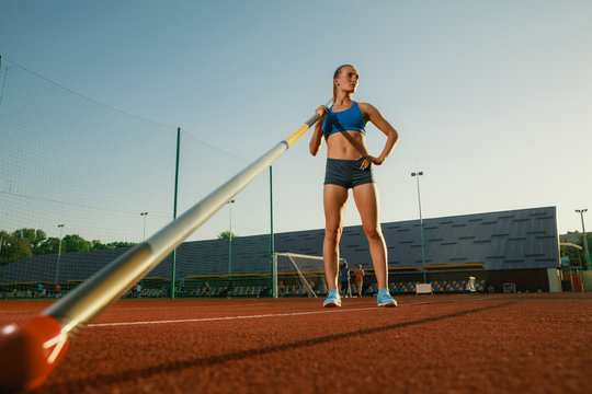 Professional female pole vaulter training at the stadium in sunny day. Fit female model practicing in high jumps outdoors. Concept of sport, activity, healthy lifestyle, action, movement, motion.