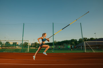 Professional female pole vaulter training at the stadium in sunny day. Fit female model practicing...