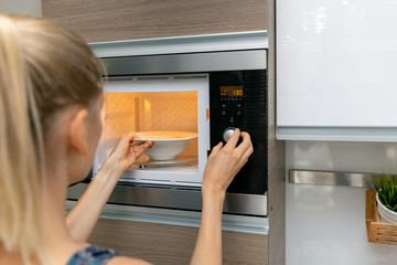 woman warm up the food in microwave oven at home - obrazy, fototapety, plakaty