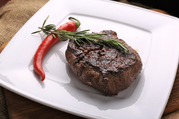 Well-done steak with chili pepper and cherry tomatoes on a wooden dish. Food photo for restaurant menu