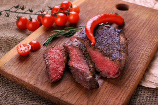 Well-done steak with chili pepper and cherry tomatoes on a wooden dish. Food photo for restaurant menu