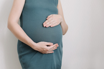 Pregnant woman in dress holds hands on belly on a white background. Pregnancy, maternity, preparation and expectation concept. 