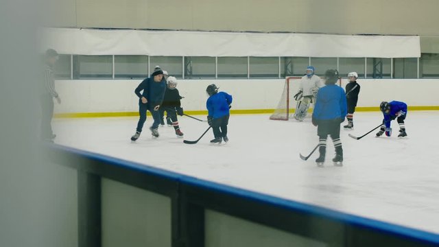 Coach training kid hockey team, showing positions and technique of stickhandling on covered ice arena