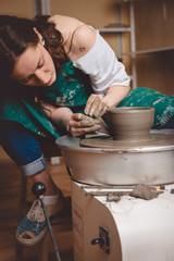 Artisan woman working on pottery wheel and making a pot.