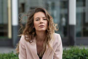 close-up portrait of a beautiful natural girl with flowing hair in a coral jacket. On the street against the glass showcases of the business center. Summer day.