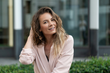 Fototapeta premium close-up portrait of a beautiful natural girl with flowing hair in a coral jacket. On the street against the glass showcases of the business center. Summer day.
