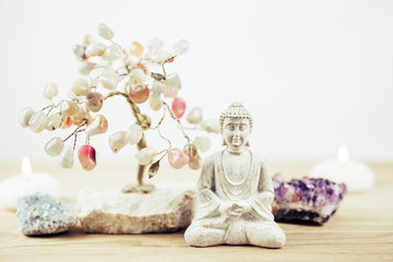 Calming meditation background with sitting meditating Buddha, crystal clusters( purple amethyst and blue celestite) and gemstone wire tree white minimalist background with copy space.