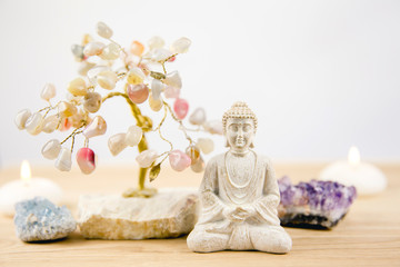 Calming meditation background with sitting meditating Buddha, crystal clusters( purple amethyst and blue celestite) and gemstone wire tree white minimalist background with copy space.