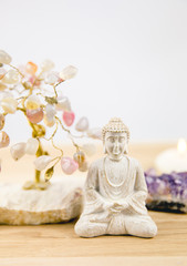 Calming meditation background with sitting meditating Buddha, crystal clusters( purple amethyst and blue celestite) and gemstone wire tree white minimalist background with copy space.