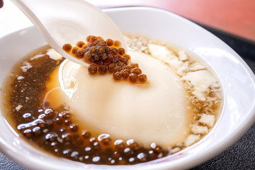 Popular Taiwan gourmet - Dessert of tapioca pearl ball (bubble) mixed bean curd tofu pudding (douhua, dou hua) in white bowl, close up, lifestyle