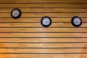 three round black clocks on the wall of wooden light gray yellow boards. horizontal lines. natural surface texture