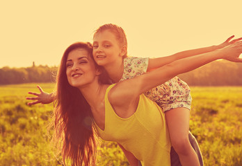 Happy enjoying mother hugging her playful laughing kid girl on sunset bright summer background. Closeup