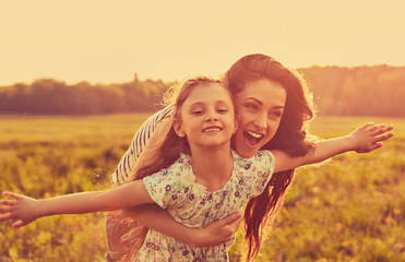 Happy enjoying mother hugging her playful laughing kid girl on sunset bright summer background. Closeup