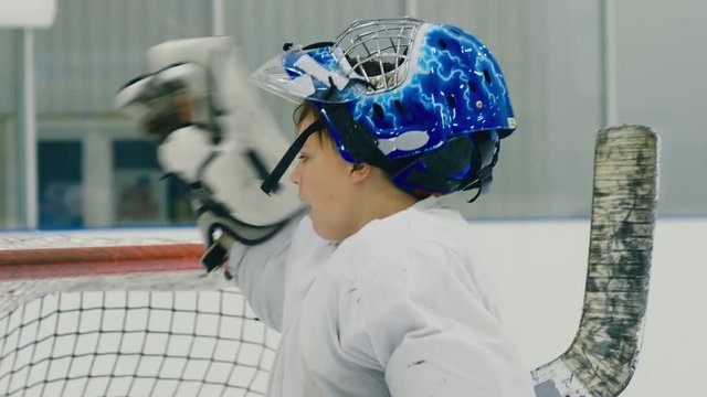 Small hockey goalie on his post taking off his helmet to drink water and coming back to position