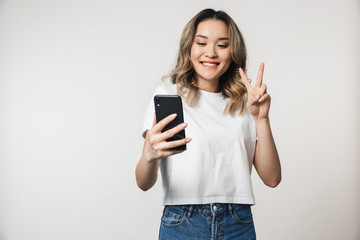 Fototapeta premium Cute young woman posing isolated over white wall background talking by mobile phone.