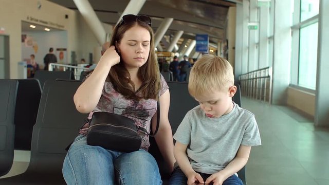 Mother with a child sitting in the departure lounge on the benches and await your flight, boy is played to the phone. Mother and son travel by plane. Tedious waiting for the flight in the waiting room