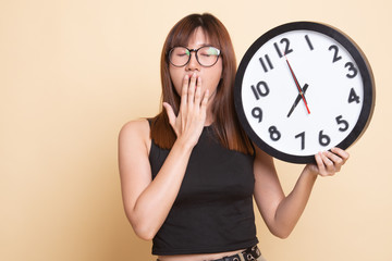 Sleepy young Asian woman with a clock in the morning.