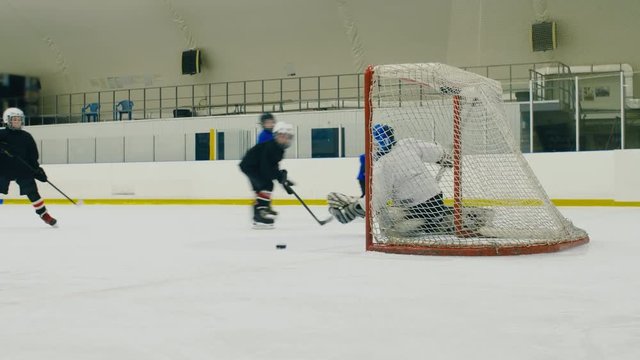 Small ice hockey players passing the puck near goal post but shooting wide