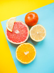 Flat lay of cut ripe juicy grapefruit, lemon and orange on yellow and blue background. Citrus pattern.