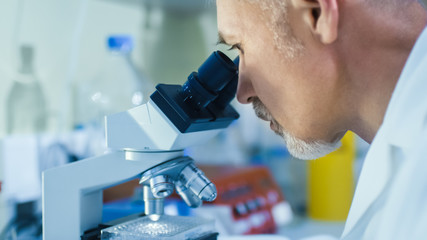 Close-up Portrait Shot of a Male Genetic Research Scientist Working on a Microscope in a Modern...